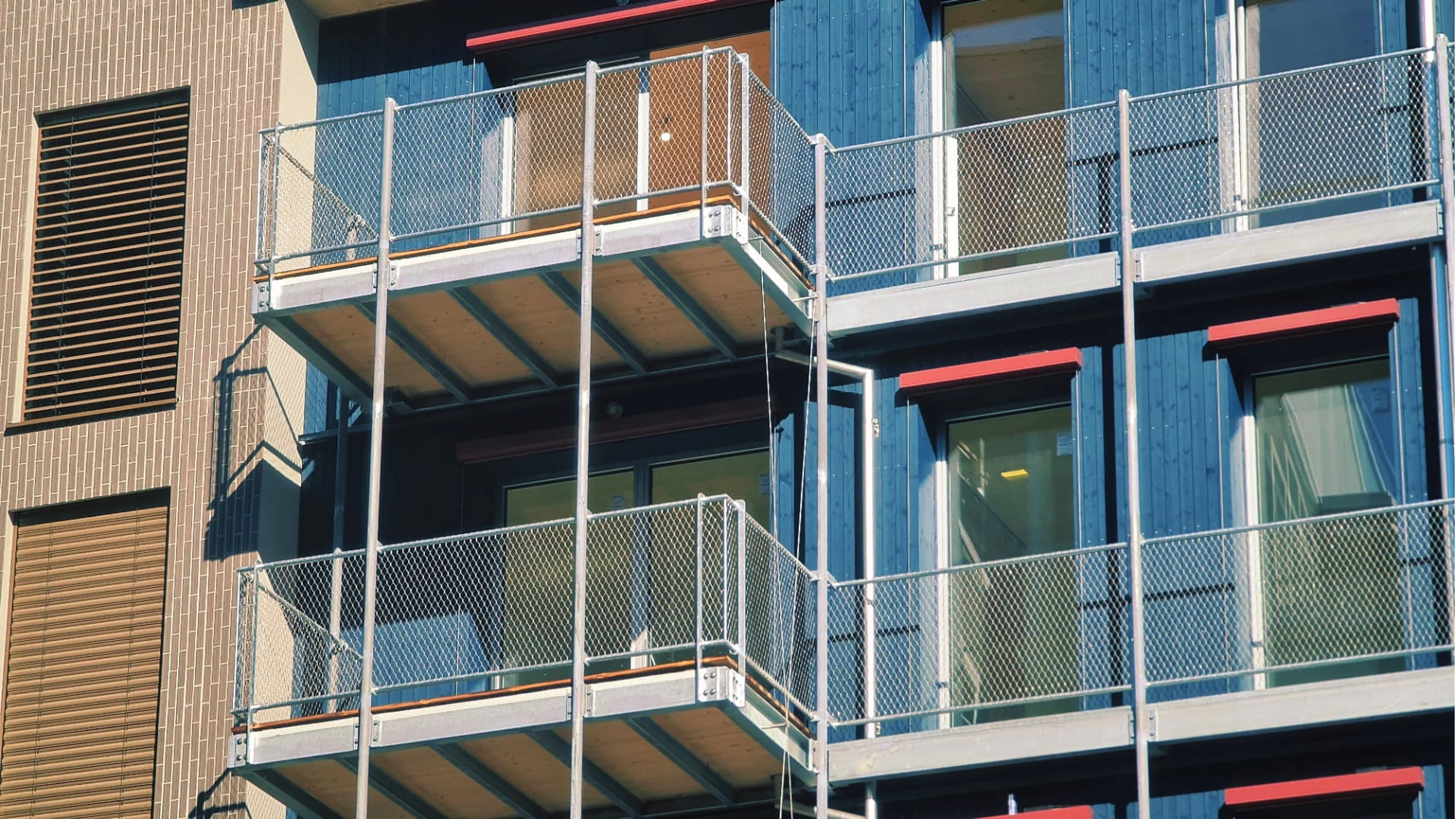 Ocynkowane konstrukcje balkonowe z balustradą z siatki przy niebieskiej drewnianej elewacji