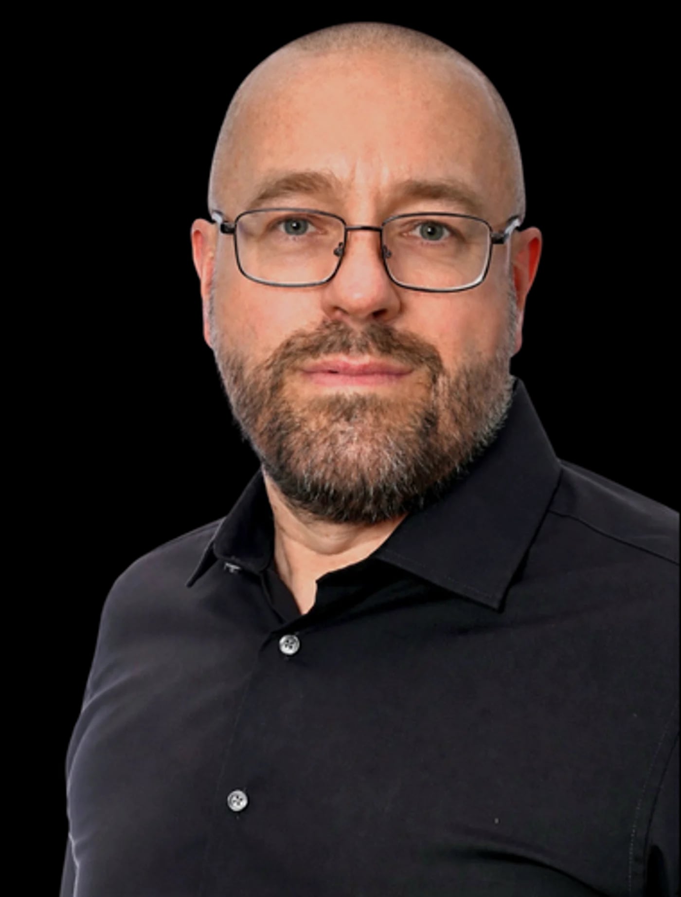 Portret mężczyzny w okularach i z brodą, w czarnej koszuli, na jasnym tle studyjnym